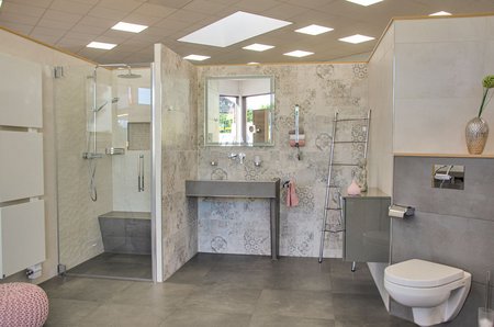 Badezimmerausstellung mit großer begehbarer Dusche, gemusterten Wandfliesen, modernem Waschtisch mit Spiegel und wandhängender Toilette.