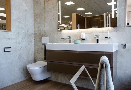 Modernes Badezimmer mit großem Doppelwaschtisch, hellen Natursteinfliesen an der Wand, integrierter Beleuchtung und wandhängender Toilette.