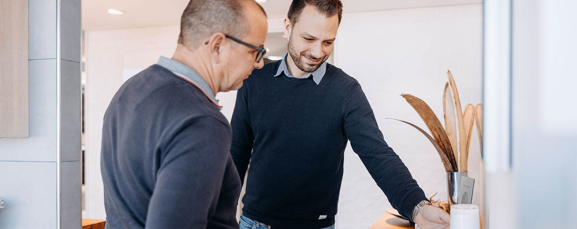 Mitarbeiter berät einen Kunden und zeigt Produkte an einem modernen Waschplatz in der Badausstellung.