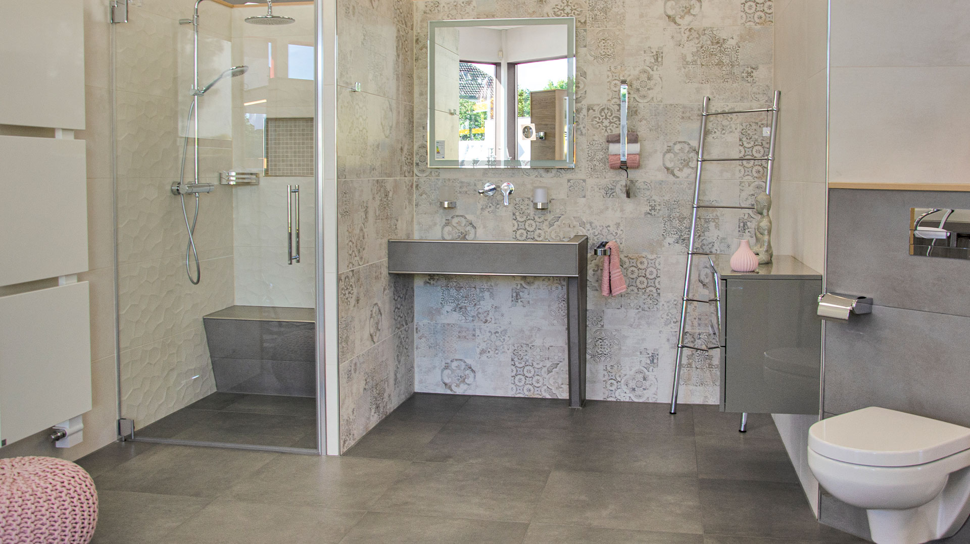 Helles Badezimmer mit großer Walk-in-Dusche, Regenbrause, grauem Waschtisch, Wandspiegel, gemusterten Wandfliesen und wandhängendem WC.